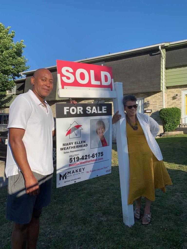 Realtor Mary Ellen Weatherhead standing next to sold sign outside house.