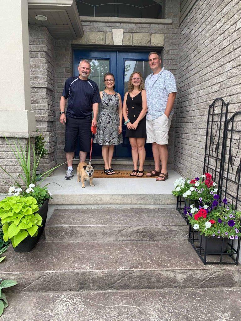 Family portrait with real estate agent, smiling homebuyers, and dog on welcoming front porch.