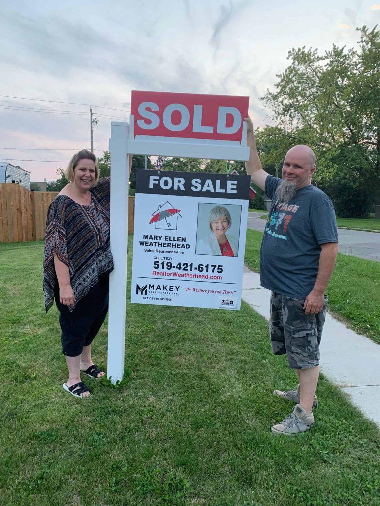 Realtor Mary Ellen Weatherhead with sold sign in front of a house for sale.