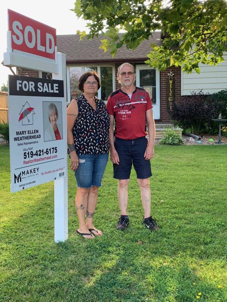 Mary Ellen Weatherhead realtor with sold sign outside home.