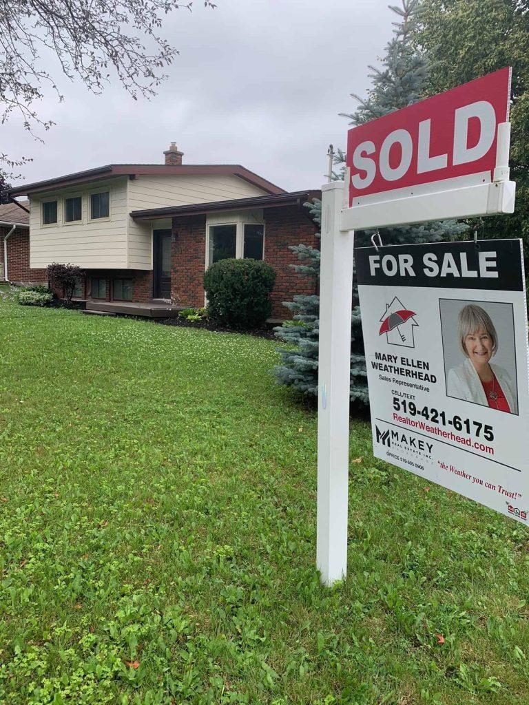 Bright sold and for sale signs outside a house with agent information and a professional photo.
